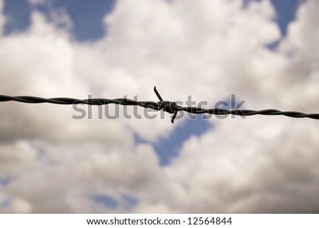 Closeup of barbed wire fence against clouds