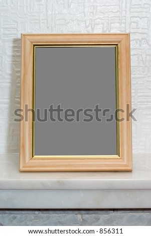 A vertical wooden picture frame blank with a clipping path included to insert a picture of choice, sitting on a marble mantelpiece against a white wall.