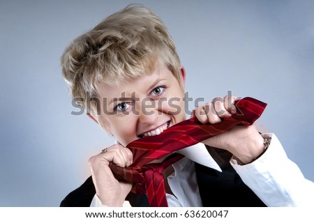 Frustrated and stressed young business woman in suit eating her necktie, studio shot.