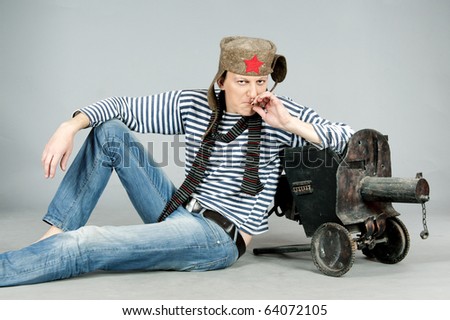 Man stylized like a Soviet soldier in World War II, sitting with old machine-gun  and smoking. Studio shot