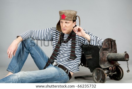 Man stylized like a Soviet soldier in World War II, sitting with old machine-gun  and smoking. Studio shot