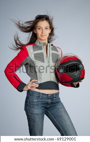 Attractive female biker with fly-away hair, dressed in jacket and holding red motorbike helmet.