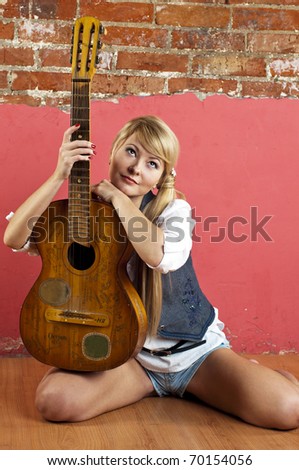 Attractive blond woman with guitar near brick wall