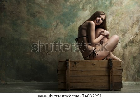 Skinny woman sitting on a wooden chest