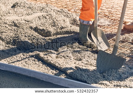 Concrete pouring during commercial concreting floors of building\
Worker with gum boots spreading ready mix concrete