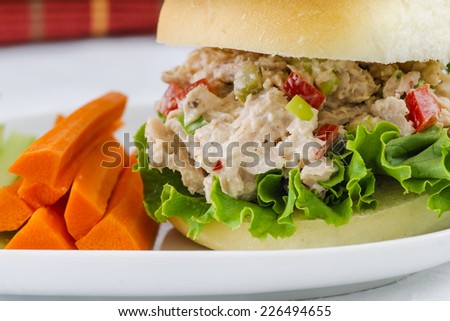 Tuna salad sandwich with lettuce on a homemade bun with healthy carrot and celery sticks and a pickle