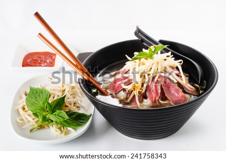 Pho - Vietnamese Rare Beef noodle soup on white background with Hoisin Sauce, Hot sauce, spices, beansprouts, and fresh basil