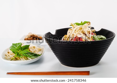 Pho - Vietnamese Rare Beef noodle soup on white background with Hoisin Sauce, Hot sauce, spices, beansprouts, and fresh basil