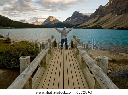 Man with hood on a bridge with arms raised to the sky