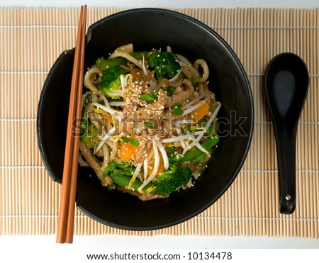 Asian stir fry with Shanghai noodles, pork, vegetables, bean sprouts and sesame seeds, with chopsticks on bamboo mat