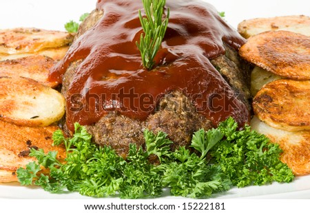 Meatloaf with fresh herbs, tomato sauce, and pan fried potatoes on white serving platter.