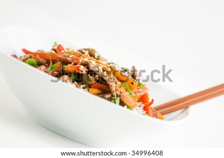 Asian beef stir-fry on rice with peppers carrots onions and peas in black bean sauce