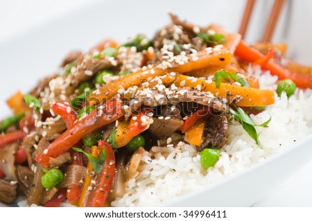 Asian beef stir-fry on rice with peppers carrots onions and peas in black bean sauce