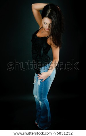 Beautiful young woman in blue jeans and black top on black background