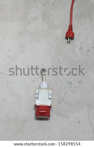 Waiting to be plugged, red electrical cable and power plug over the gray, stucco wall