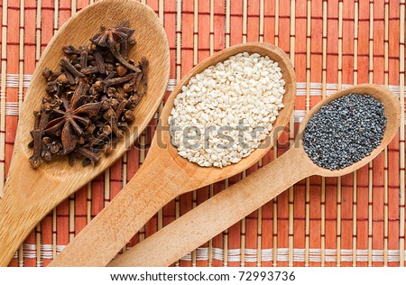 Cooking spices in wooden spoons. Cloves, sesame seeds, poppy seeds.