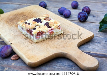 Fresh plum cake on cutting board and fresh plums on wooden old table