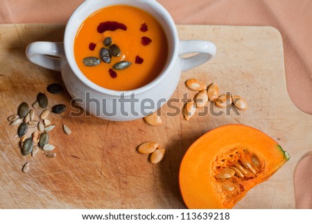 Pumpkin vegetable cream soup in white bowl with pumpkin and seeds on cutting board