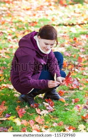 Beautiful woman in the autumn park collects red and yellow leaves