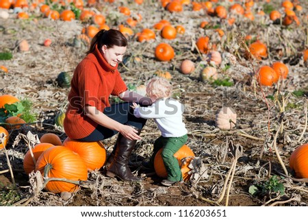 Little toddler boy and his mother in a field of big orange pumpkins on sunny day