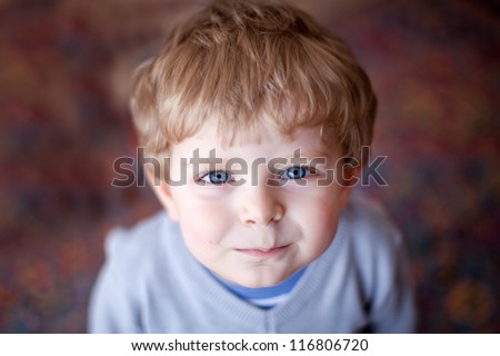 Portrait of adorable toddler boy with blond hairs and blue eyes smiling