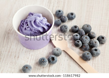 Serving of frozen creamy ice yogurt  with whole fresh blueberries and wooden spoon