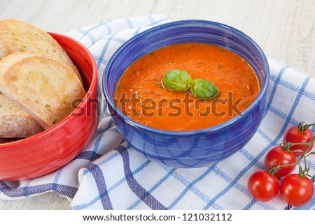 Fresh cream tomato soup with organic garlic and tomatoes in blue bowl and baked bread in red bowl