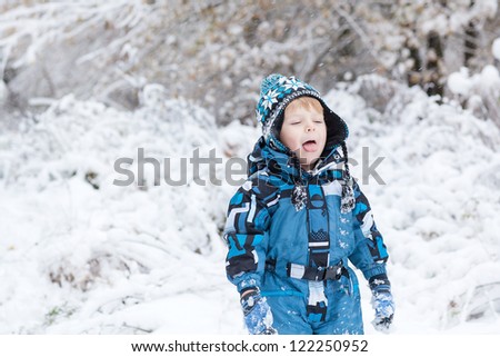 Beautiful little boy having fun with snow outdoors on beautiful winter day in forest
