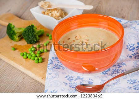 Fresh cream broccoli and pea soup in orange bowl with vegetables and roasted almonds