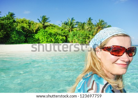 Young woman on boat with white sand beach on Maldivian island on background