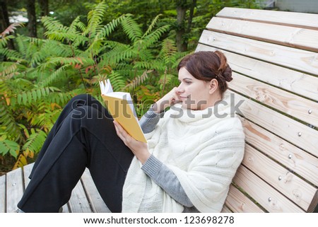 Beautiful woman reading book on bench in spring park