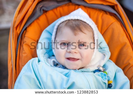 Little baby boy in spring clothes and orange pram outdoor