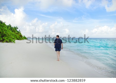 Young man walking on white sand beach on Maldivian island