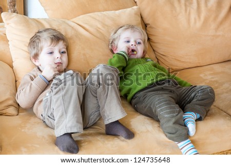 Two little brother boys watching tv and eating candy indoor