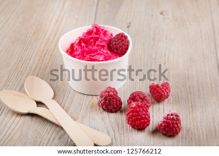 Serving of frozen creamy ice yoghurt  with whole fresh raspberries and wooden spoon