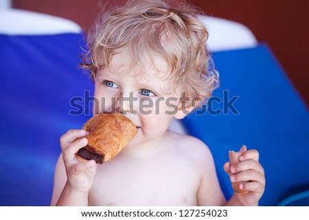 Adorable toddler boy with dirty chocolate face smiling eating croissant