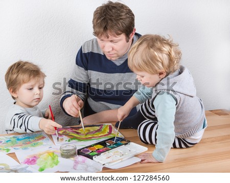 Father and two little boys siblings having fun painting at home