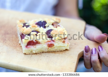 Fine fresh baked plum cake on wooden board holding by woman hand