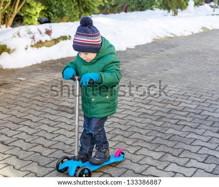 Little toddler boy learning to drive scooter outdoors