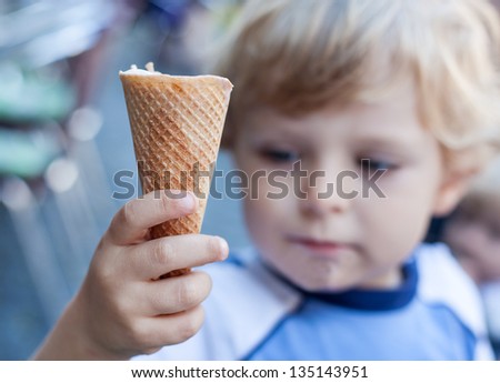 Little toddler boy eating ice cream in cone in summer. Selective focus on ice cream.