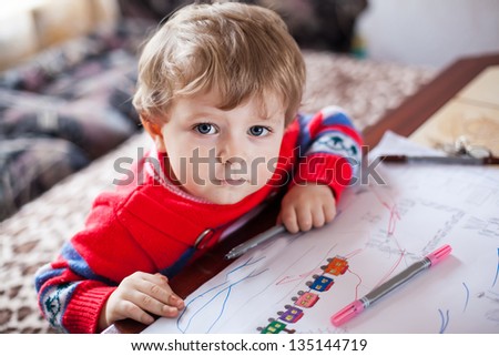 Little toddler boy with blue eyes drawing indoor with colorful pens
