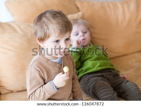 Two little brother boys watching tv and eating candy indoor. Selective focus on child on foreground.