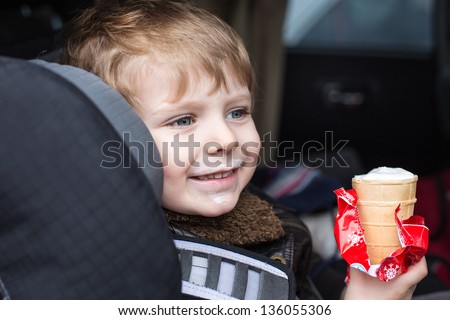Adorable toddler boy with blue eyes in safety car seat eating sweet ice cream