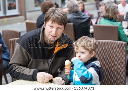 Young father and little boy eating ice cream in cafe