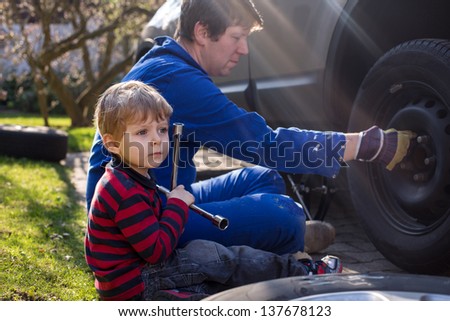 Boy of three years and his father changing wheel on car with pneumatic wrench