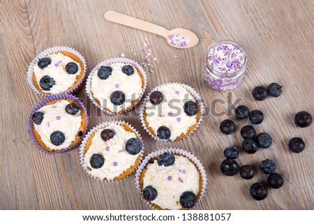 Tasty sweet muffins with blueberries, cream and fresh berries on wooden background