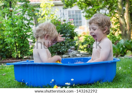 Two little brothers having fun with water in summer garden on sunny day