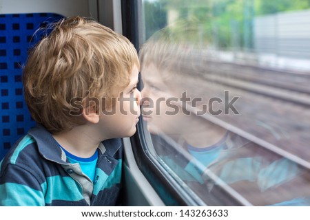 Sweet toddler boy looking out train window outside, while it moving. travel