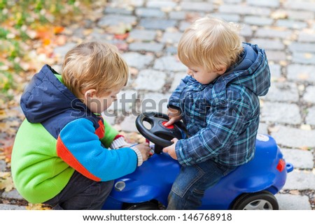 Two toddler boys playing with car in autumn park