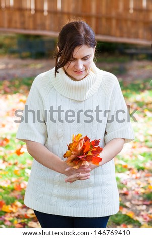 Beautiful girl in the autumn park collects red and yellow leaves